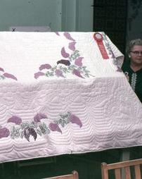Two Women Next to White Quilt With Embroidered Wisteria