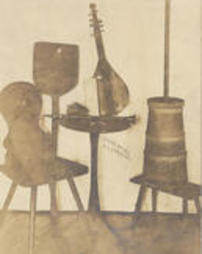 Chair, bread peel, table with, clarinet, music, string instrument, bitter churn sitting on a stool.